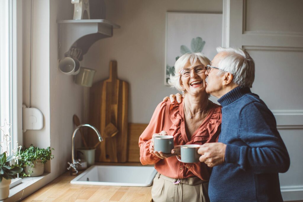 Photo of a senior man giving his wife a kiss while having coffee