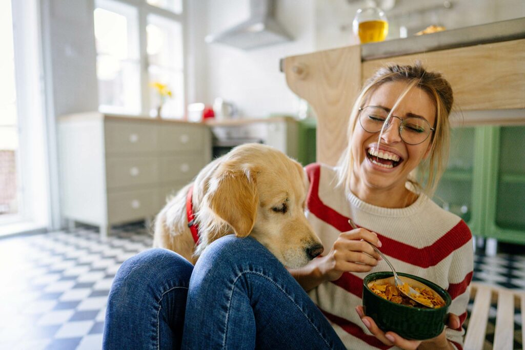 Photo of a woman trying to eat cereal while her Golden Retriever tries to eat it as well